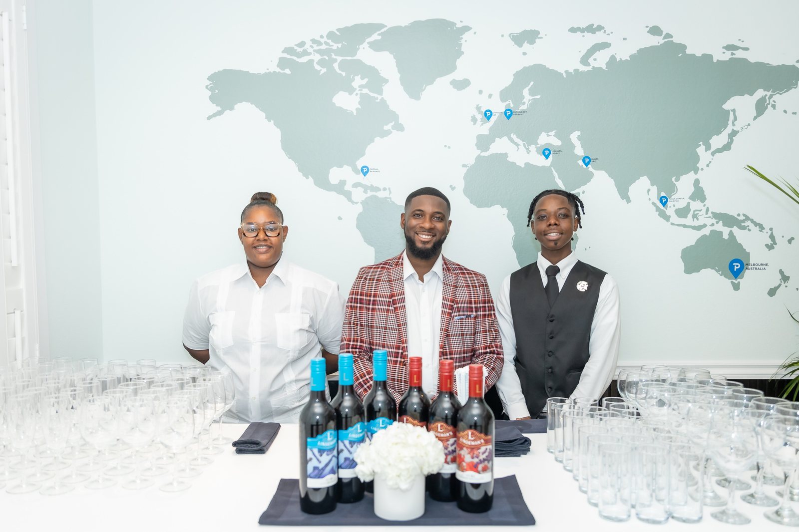 Top Tier Butlers team at a bar with wine bottles and glassware in front of a world map wall