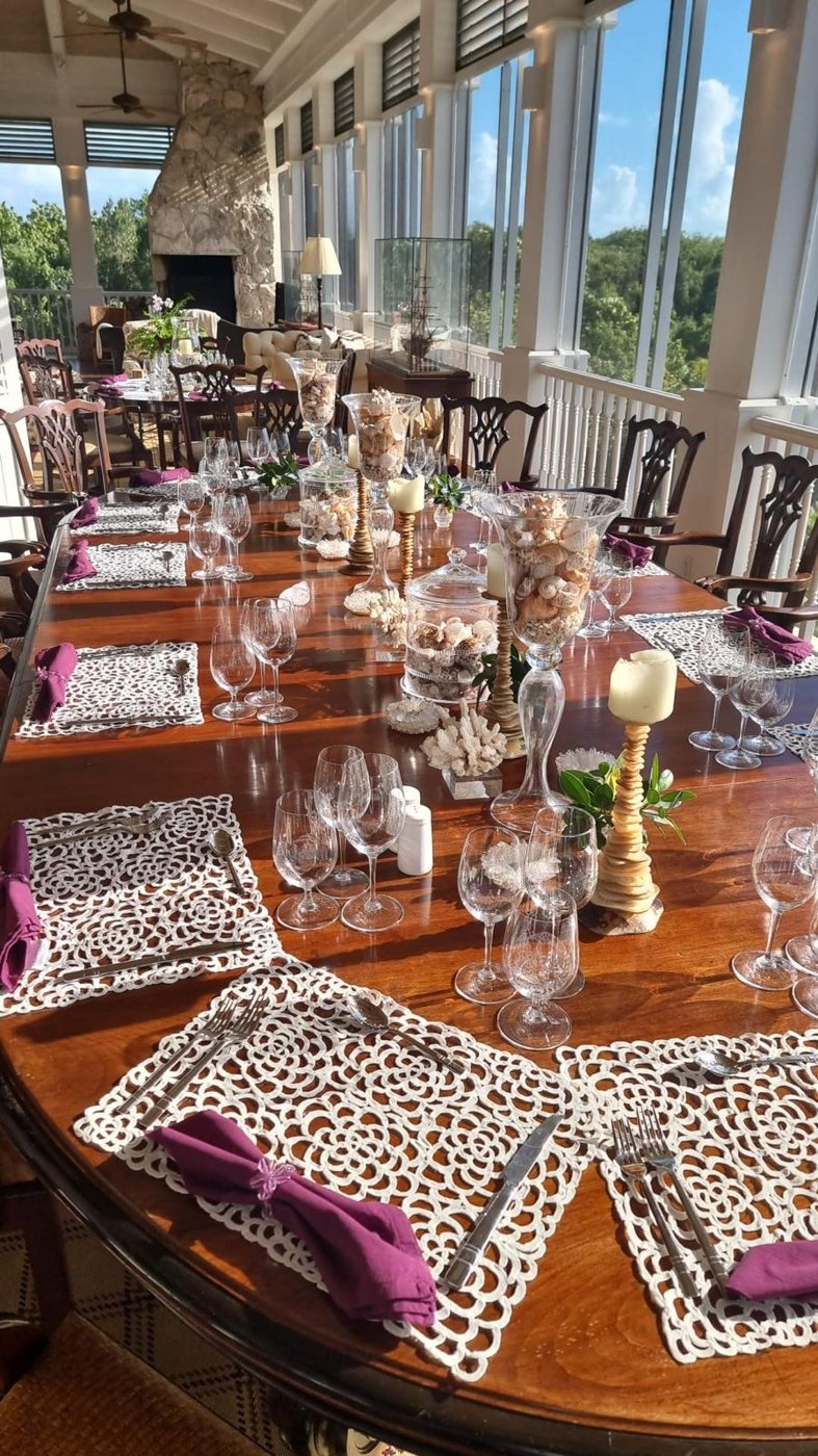 Long veranda dining table dressed with crystal glassware, lace placemats and shell centrepieces