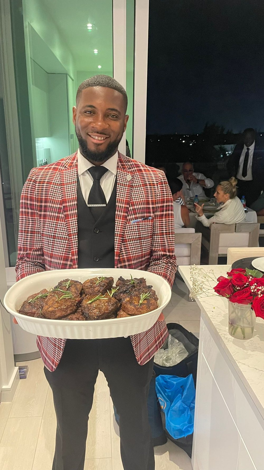 Top Tier Butler in a tailored plaid jacket presenting a dish at an evening dinner