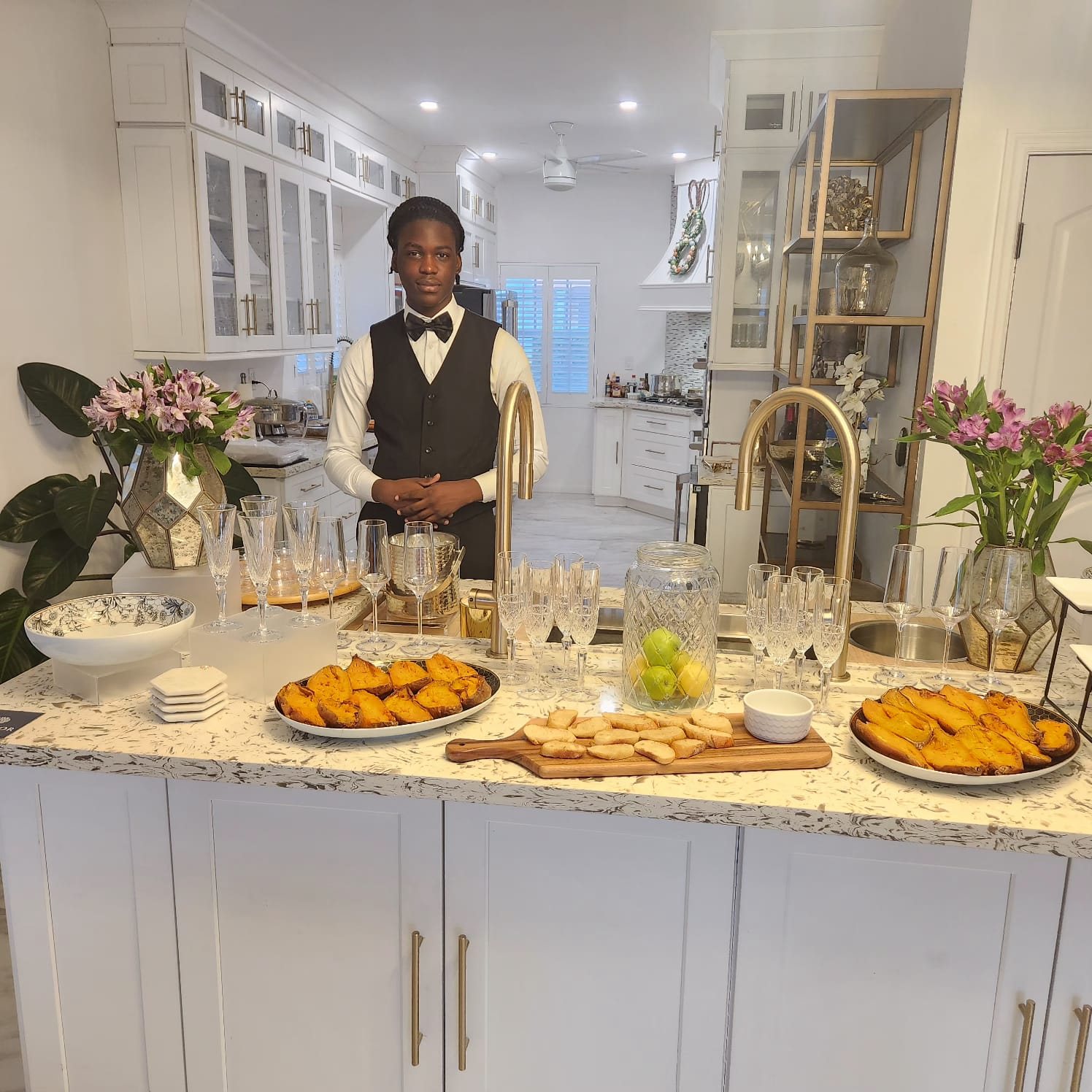 Top Tier Butler standing behind a prepared kitchen spread with crystal glassware and fresh flowers
